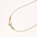 Delicate white beaded necklace with central freshwater pearl and gold-toned emerald accents on white background.