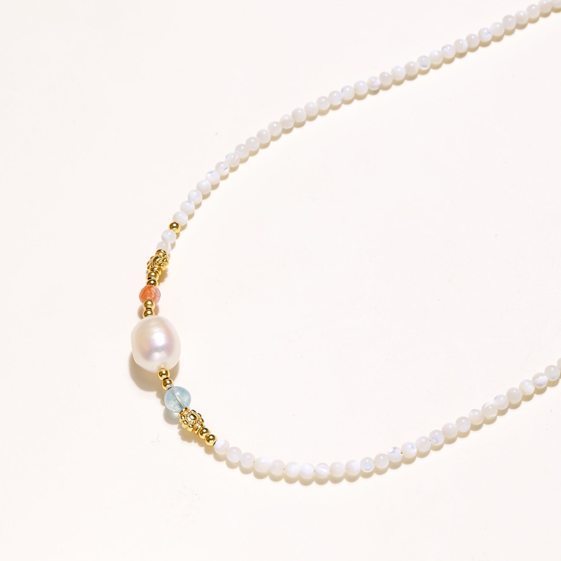 Delicate white beaded necklace with central freshwater pearl and gold-toned emerald accents on white background.