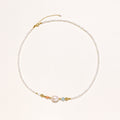 Delicate white beaded necklace with central freshwater pearl and gold-toned emerald accents on white background.