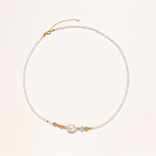 Delicate white beaded necklace with central freshwater pearl and gold-toned emerald accents on white background.