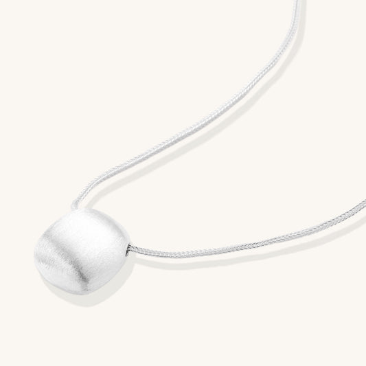 Minimalist sterling silver necklace with brushed square pendant on adjustable chain against white background.