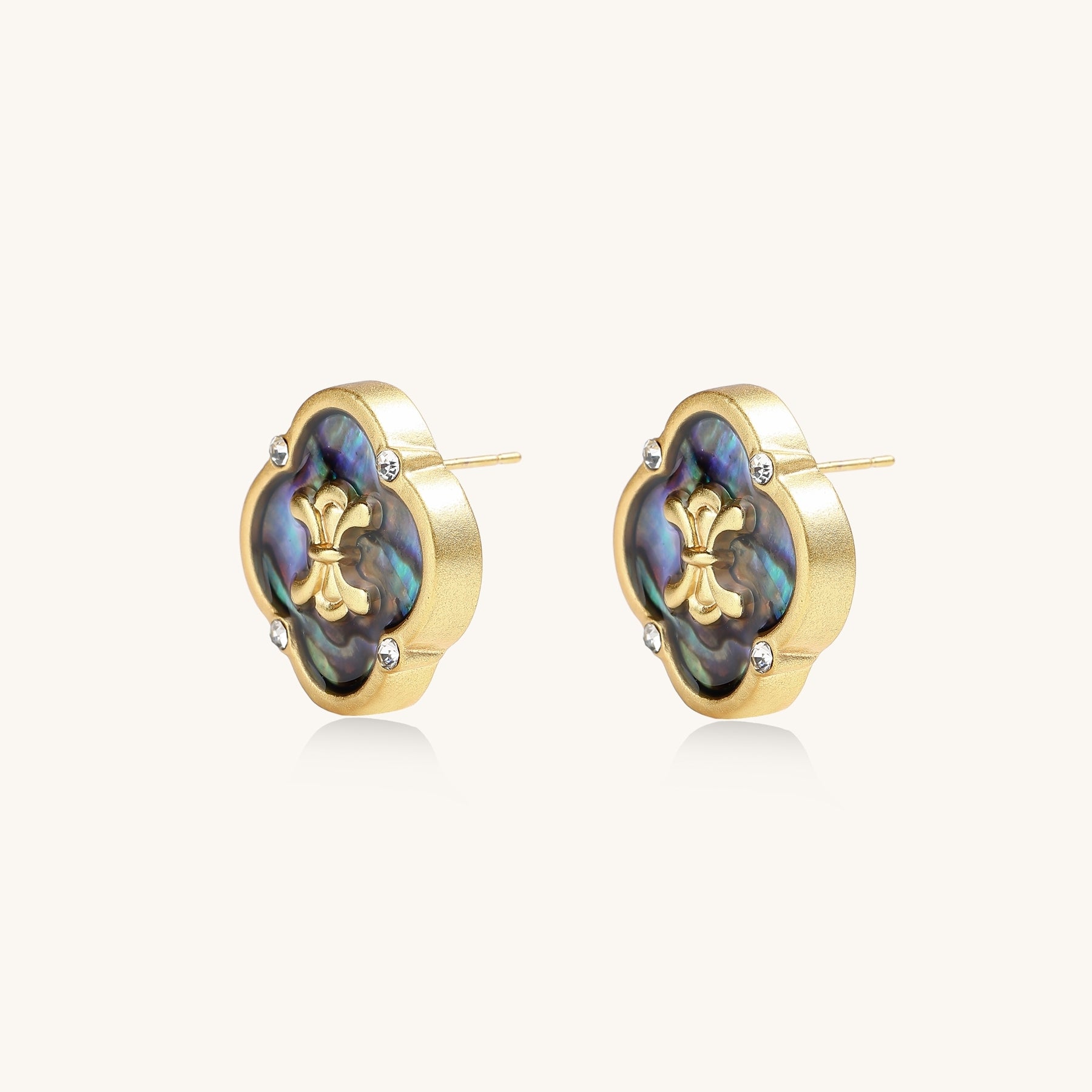 Gold-plated quatrefoil stud earrings featuring iridescent abalone shell centers with decorative motifs and crystal accents