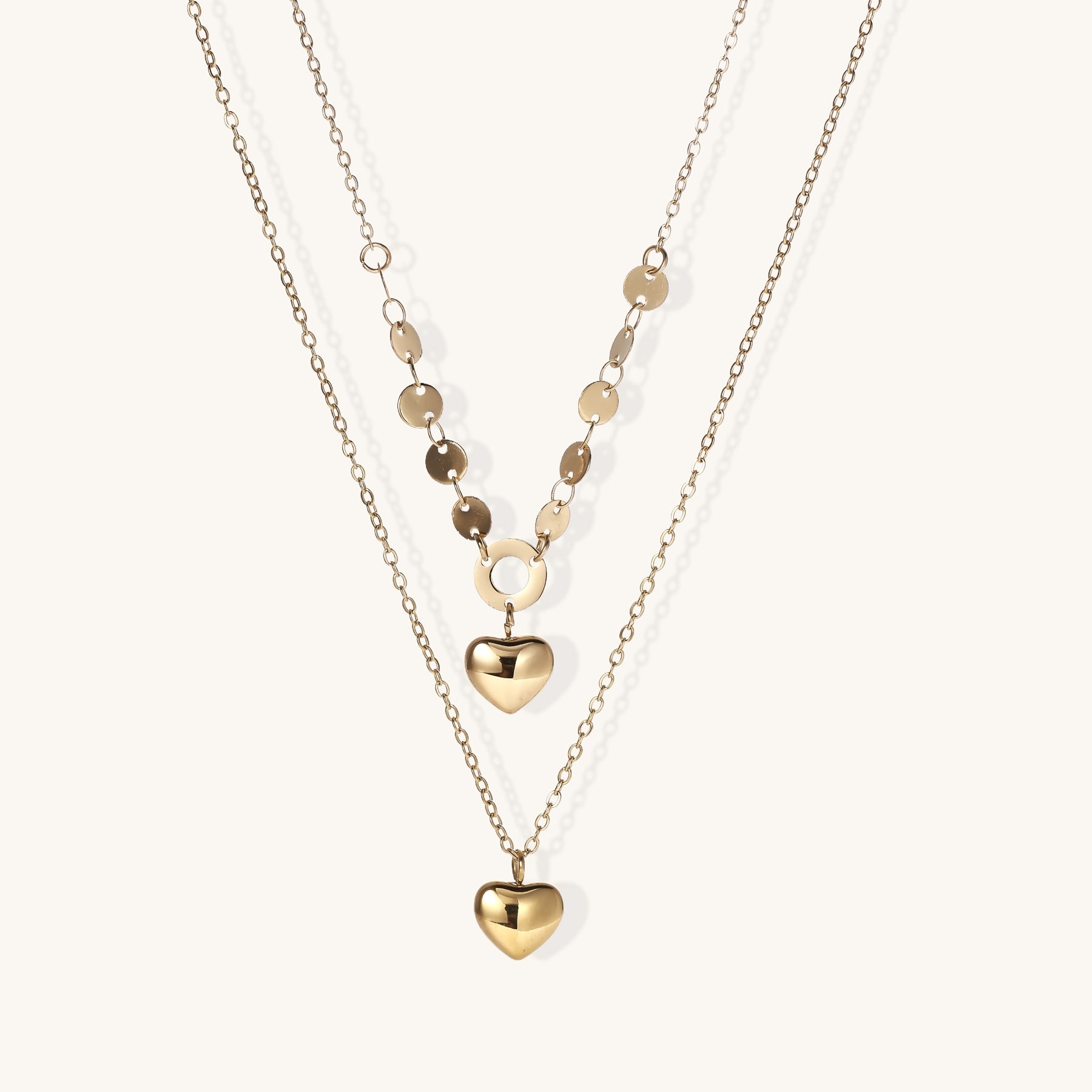 Three-layer gold-plated necklace set with disc chain and two heart pendants on neutral background