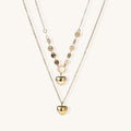 Three-layer gold-plated necklace set with disc chain and two heart pendants on neutral background