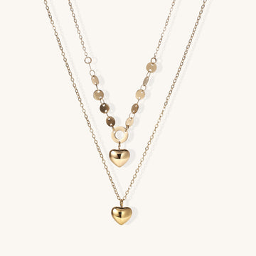Three-layer gold-plated necklace set with disc chain and two heart pendants on neutral background