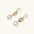 Gold-plated sunburst flower earrings with baroque pearl drops and textured metal caps on neutral background.