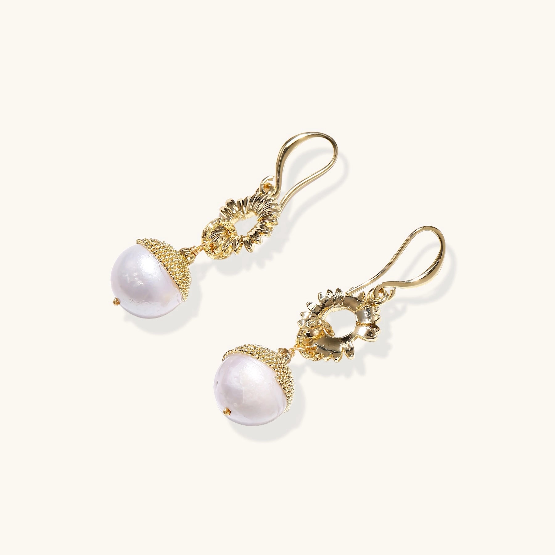 Gold-plated sunburst flower earrings with baroque pearl drops and textured metal caps on neutral background.