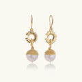 Gold-plated sunburst flower earrings with baroque pearl drops and textured metal caps on neutral background.