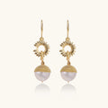 Gold-plated sunburst flower earrings with baroque pearl drops and textured metal caps on neutral background.