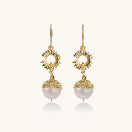 Gold-plated sunburst flower earrings with baroque pearl drops and textured metal caps on neutral background.
