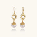 Gold-plated sunburst flower earrings with baroque pearl drops and textured metal caps on neutral background.
