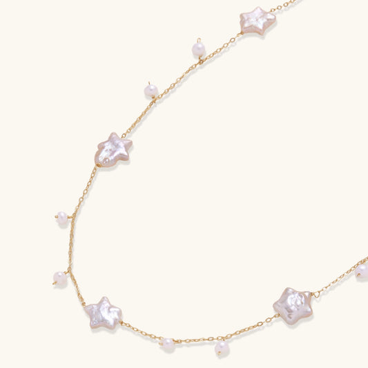 Delicate gold chain necklace with star-shaped baroque pearls and small freshwater pearls on cream background.