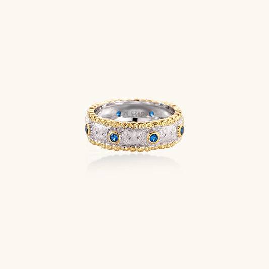 Sterling silver ring with brushed center band, blue zirconia stones, and 24k gold-plated decorative borders.