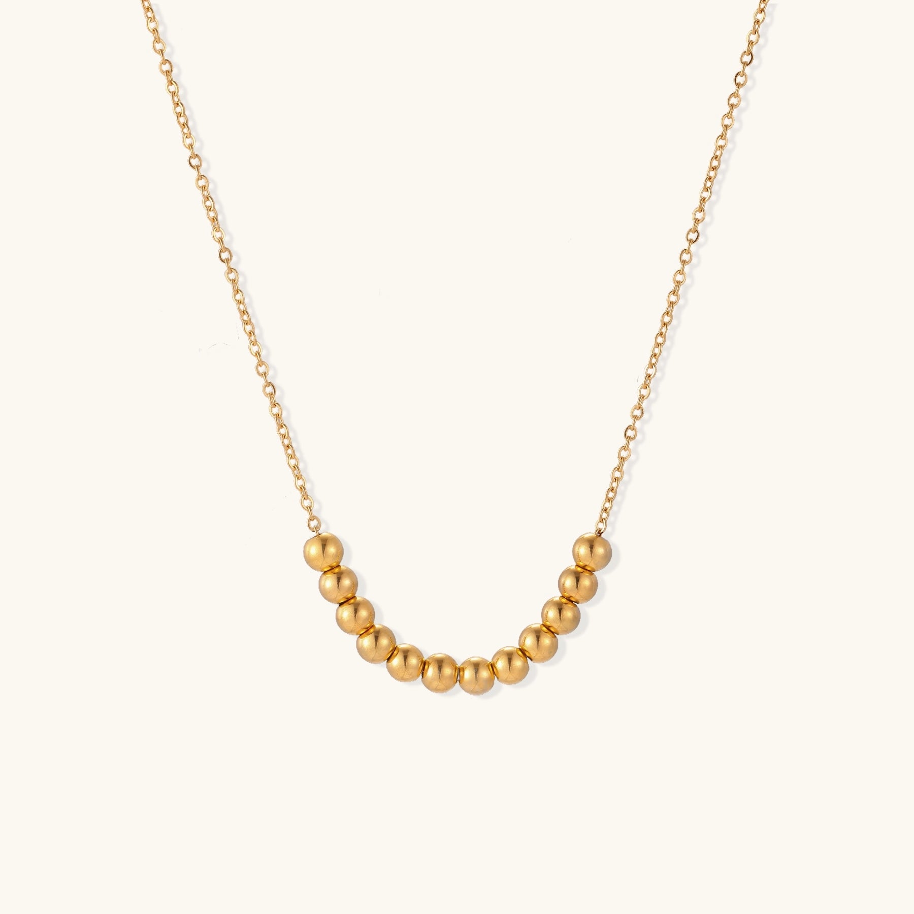 Delicate gold-plated chain necklace featuring clustered spherical beads arranged in elegant curve against white background.