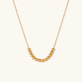 Delicate gold-plated chain necklace featuring clustered spherical beads arranged in elegant curve against white background.