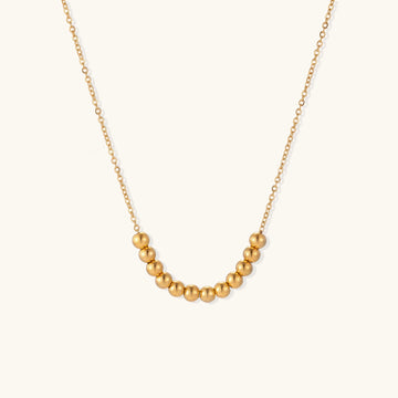 Delicate gold-plated chain necklace featuring clustered spherical beads arranged in elegant curve against white background.